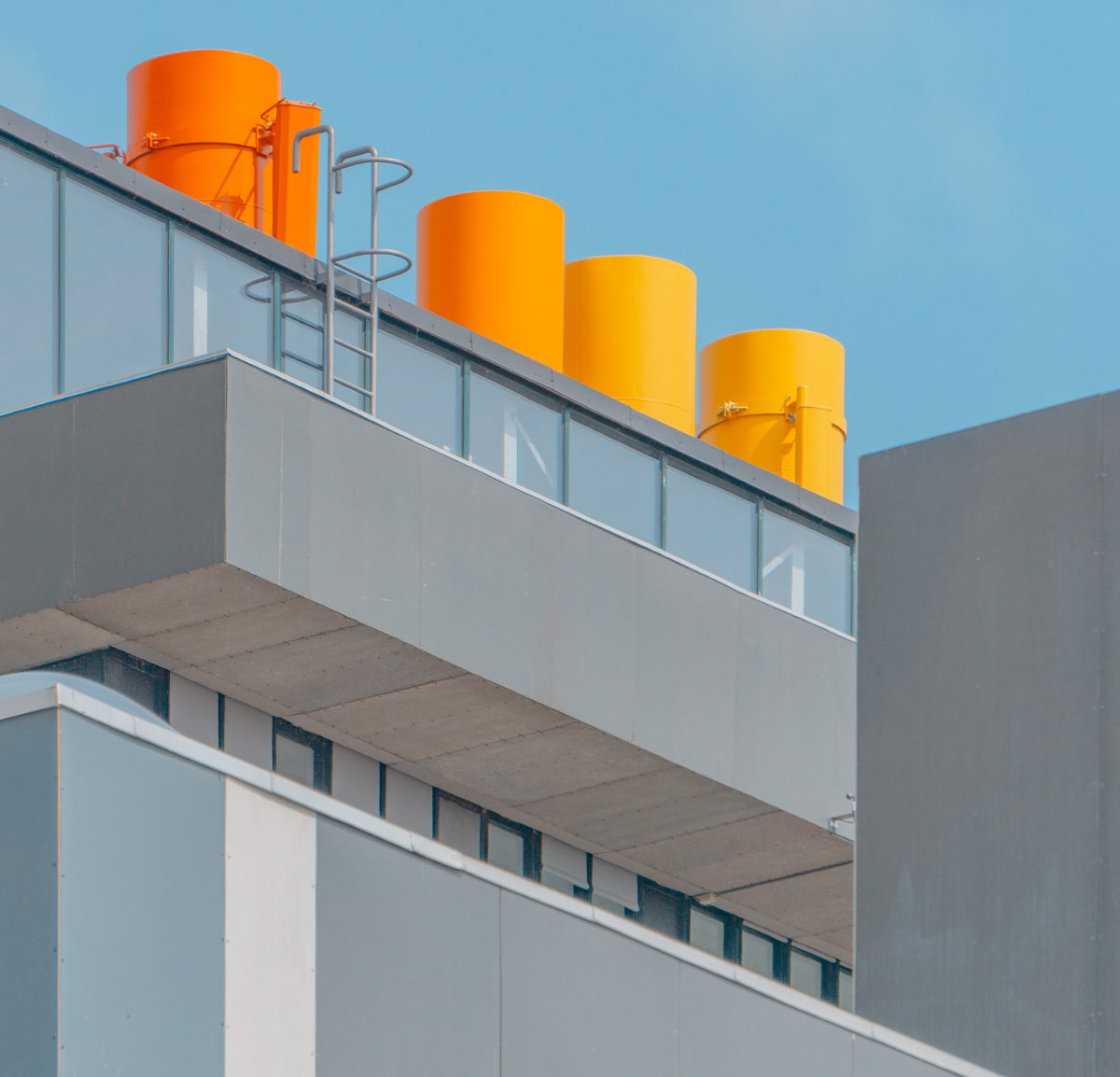 Vertical shot of a glass building with orange chimneys under the blue sky